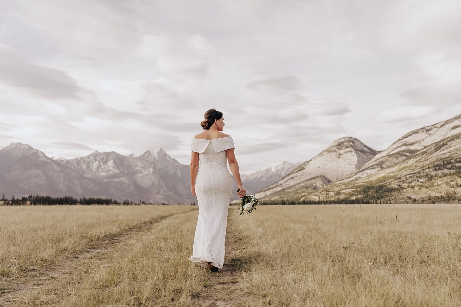 Jasper elopement photographer. Portraits of bride and groom in a field with mountains in the background.